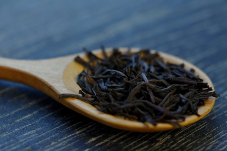 dry black tea leaves on a wooden spoon on a dark background macro close-up