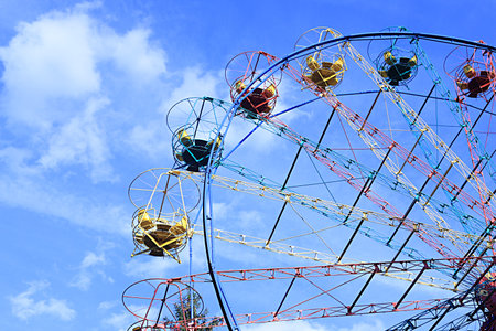 multi-colored cabins of the Ferris wheel against the background of a blue sky with clouds. copy spaceの写真素材