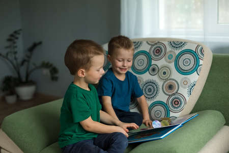 Children at home look at a book on the sofa.