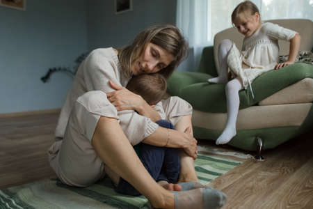 Mom at home sitting on the floor hugs and plays with the children.の写真素材