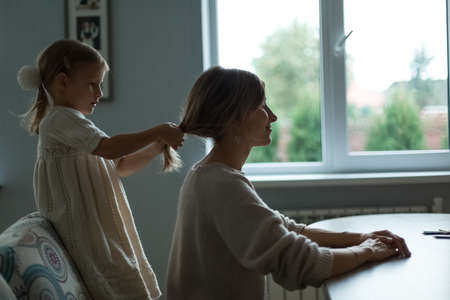 The daughter braids her mothers hair. Home furnishings.の写真素材