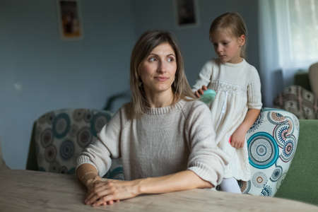 The daughter braids her mothers hair. Home furnishings.