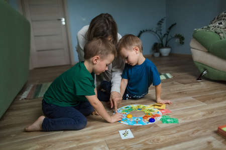 Mother with children playing a board game on the floor.