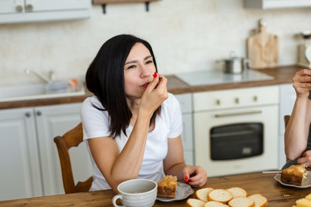 Brunette girl is drinking tea with sweets, at home in the kitchen.の写真素材
