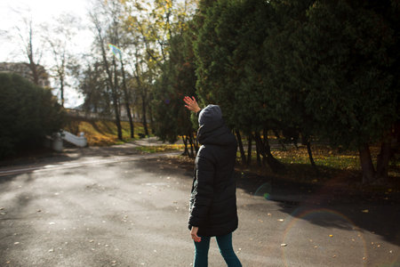 A girl in the park in warm clothes and a hat, on a sunny day.