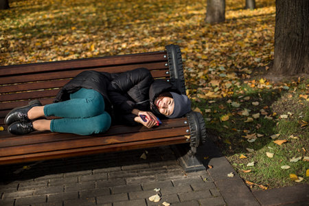 Young girl in warm clothes lies in the park on a bench smiling
