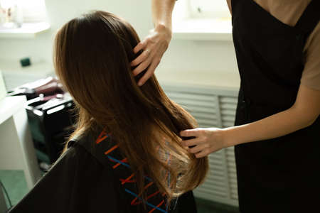 Hands touch someone elses brunette hair in a beauty salon.