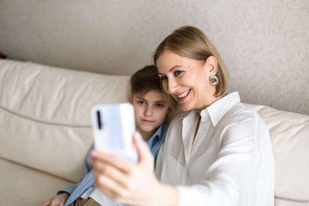 Boy and adult woman take a selfie on the phone while sitting on the couch.の写真素材