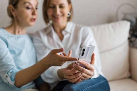 Two women are sitting on the couch and looking at the phone while talking.の写真素材