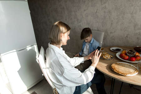 Woman and child are sitting at table in kitchen and looking at their phones.の写真素材
