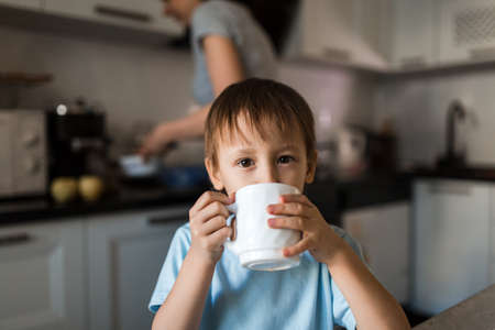 Child is drinking tea from mug and looking at camera.の写真素材