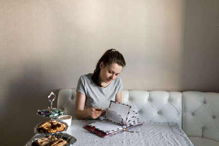 The girl in the kitchen sits on the couch at the table, leafs through a notebook