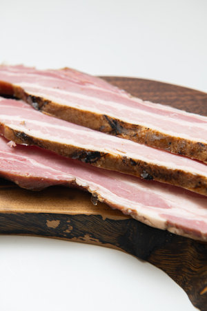 Slices of smoked bacon on a wooden board, isolated on whiteの写真素材