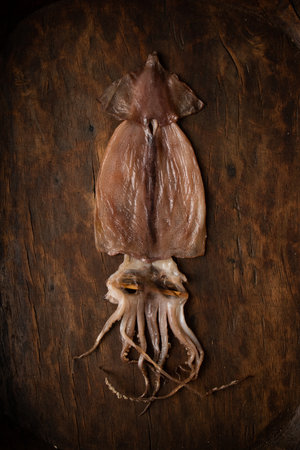 Fresh squid on a wooden cutting board. Top view. Dark background.の写真素材