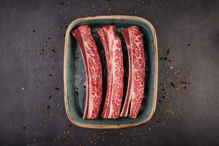 Raw fresh wagyu beef ribs in ceramic bowl on dark background, top viewの写真素材