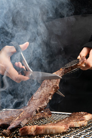 Chef cutting grilled meat on barbecue grill, close-up viewの写真素材
