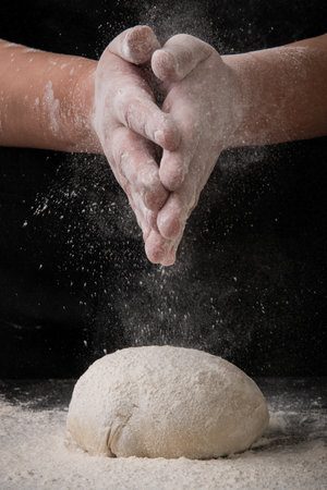 Female hands kneading dough on a black background with flour.の写真素材