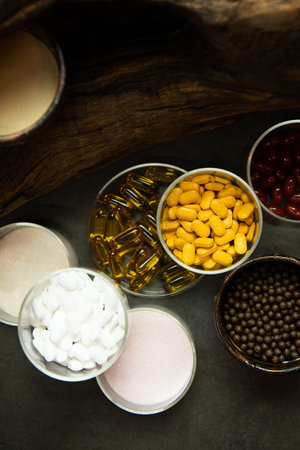 Pills, tablets and capsules in bowls on a wooden background.