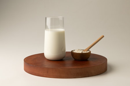 A glass of milk and a wooden spoon on a round wooden standの写真素材