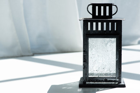 Vintage black lantern on white background with shadow and sunlight. Selective focus.