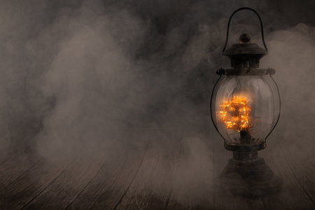 Lantern with a glowing light bulb on a dark background with smoke