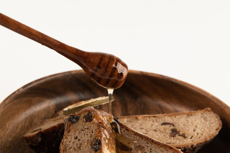 Honey dripping from a wooden honey dipper over slices of bread