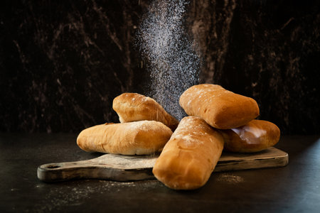 Freshly baked baguettes on a wooden board sprinkled with flour. Dark background.の写真素材