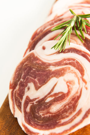 Slices of bacon on a cutting board with rosemary.の写真素材