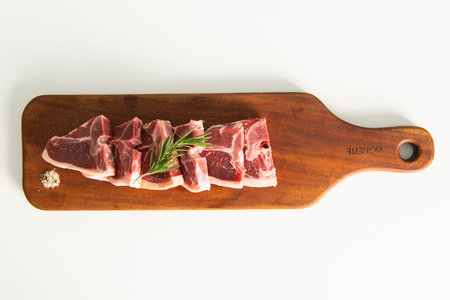 Raw lamb chops with rosemary on wooden cutting board isolated on white background