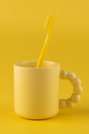 Yellow plastic toothbrush in a yellow mug on a yellow background.の写真素材