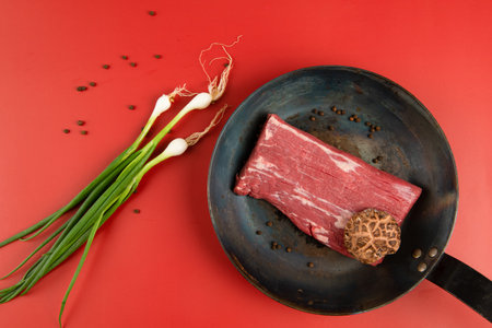 Raw beef steak in a frying pan on a red background, top viewの写真素材
