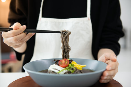 Asian woman in white apron holding black noodle and chopsticks.の写真素材