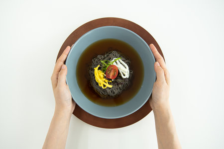 Top view of female hands holding bowl of black noodle soup on white backgroundの写真素材