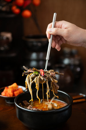 Hands of woman eating spicy noodles with beef in black bowl