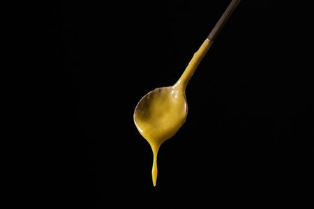 A spoon dripping with yellow sauce against a black backgroundの写真素材