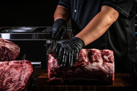 Butcher's hands in black gloves cutting raw meat on a wooden board.の写真素材