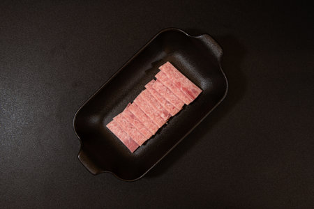 Raw pork on a black plate on a black background, top view