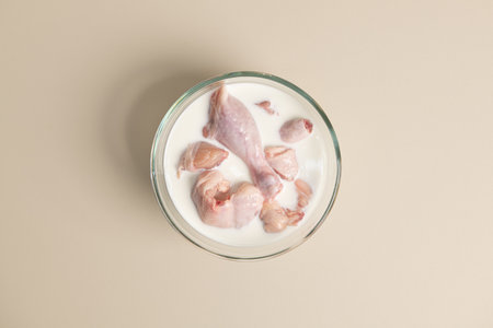 Raw chicken legs in a glass of milk on a beige backgroundの写真素材