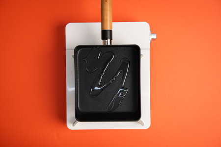 A black frying pan with a wooden handle on a white stand against an orange background.
