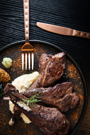 Grilled beef steaks with mashed potatoes and herbs on black wooden table
