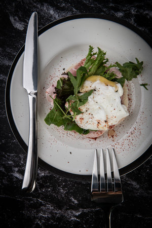 Poached eggs with ham and arugula salad on white plateの写真素材