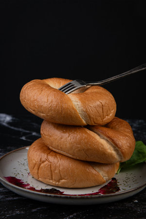 Freshly baked bagels on a plate with a fork on a black background