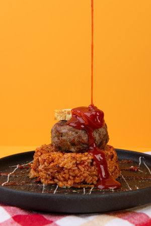 fried rice with meatballs and ketchup on a plate on an orange background