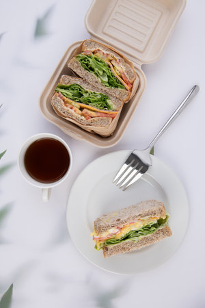 Top view of two sandwiches with ham, cheese, tomatoes and arugula served with a cup of tea