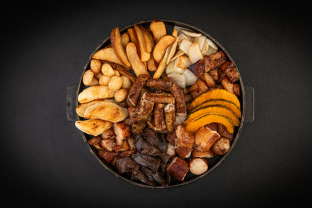 Grilled meat and vegetables in a pan on a black background.の写真素材
