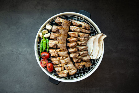 Grilled pork on barbecue grill with vegetables and spices on black background