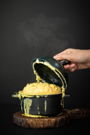 Woman's hand holding a pot with yellow butter on a black background