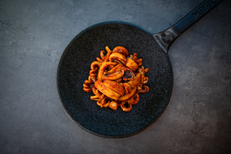 Fried squid rings in a frying pan on black stone background.