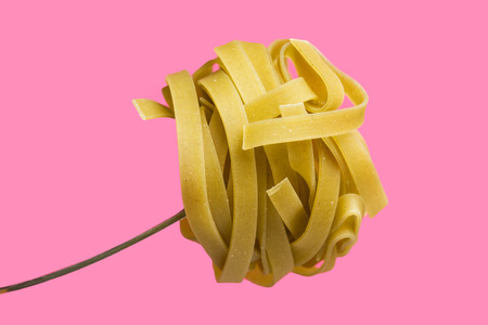 Dried spaghetti on a fork on a pink backgroundの写真素材