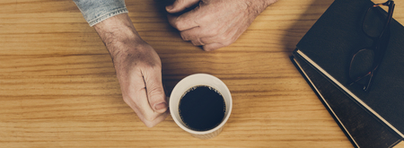 A man with a cup of coffee in his hand on a wooden table at homeの写真素材
